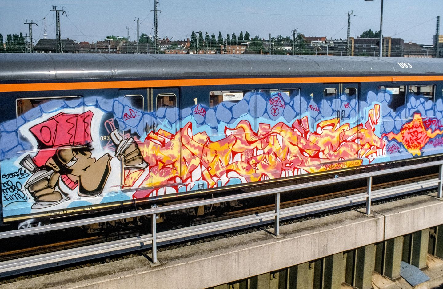 Burner auf Stahl  Der Schriftzug "Prime" weckt nicht nur farblich die Assoziation zu Feuer. Es handelt sich um einen "Burner" - ein besonders aufwendiges und qualitativ hochwertiges Bild. Das gilt sowohl für den detailreich gestalteten Schriftzug wie auch für die Figur und den Hintergrund. Dass das Werk zudem auf einer S-Bahn entstand, wertet es in der Szene noch einmal erheblich weiter auf. Das Foto erschien 1989 im stern zu einem der ersten deutschen Artikel über das Phänomen Graffiti.