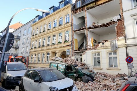 Trümmer liegen auf einem Auto vor einem Haus, dessen Fassade eingestürzt ist