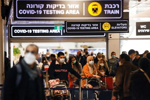 Eine Menschenmenge an einem Flughafen sowie Schilder auf Hebräisch und Englisch
