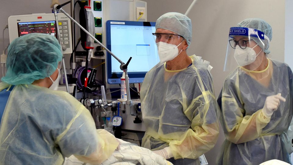 Drei Menschen in medizinischer Schutzkleidung kümmern sich um einen Menschen in einem Krankenhausbett