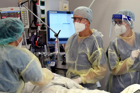 Drei Menschen in medizinischer Schutzkleidung kümmern sich um einen Menschen in einem Krankenhausbett