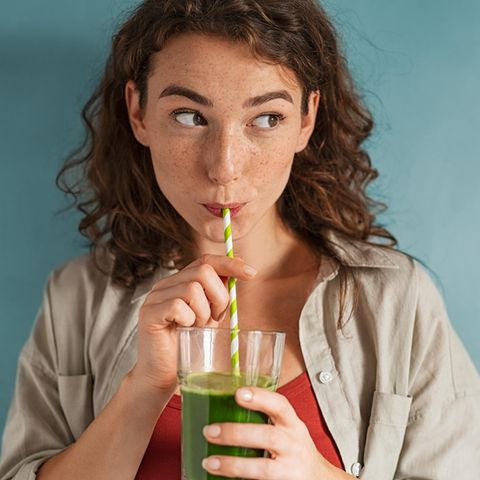 Mädchen trinkt grünen Saft aus einem Strohhalm