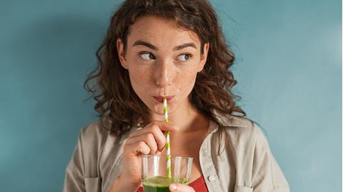 Mädchen trinkt grünen Saft aus einem Strohhalm