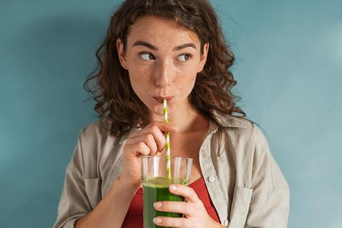 Mädchen trinkt grünen Saft aus einem Strohhalm