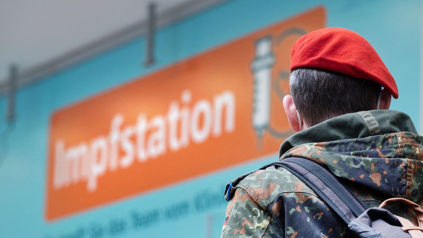 Ein Soldat in Uniform blickt auf ein Schild mit der Aufschrift "Impfstation"