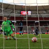 Hinter einem Tornetz kniet ein junger weißer Mann in grünem Torwart-Dress einem Ball hinterher, der ins Tor rollt