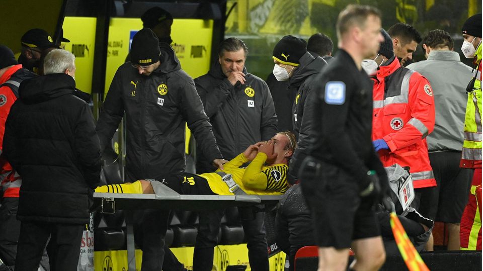 Ein Fußballer in gelb-schwarzem Trikot und schwarzer kurzer Hose wird auf einer grauen Trage vom Platz gebracht Ein Fußballer in gelb-schwarzem Trikot und schwarzer kurzer Hose wird auf einer grauen Trage vom Platz gebracht