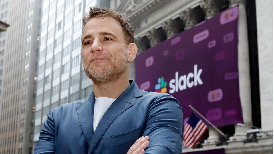 Slack founder Stewart Butterfield stands in front of a building decorated with a large poster of the Slack logo