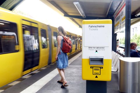 Ein Automat zum Ticketllösen steht an einem Bahnsteig, an dem eine Bahn einfährt