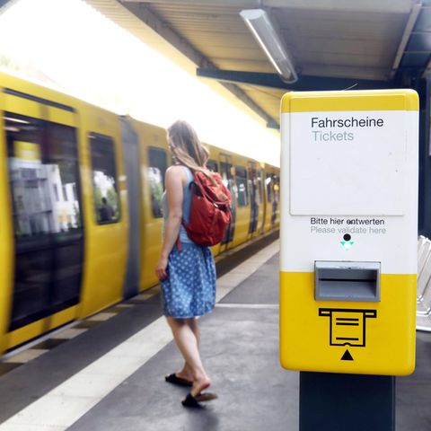 Ein Automat zum Ticketllösen steht an einem Bahnsteig, an dem eine Bahn einfährt
