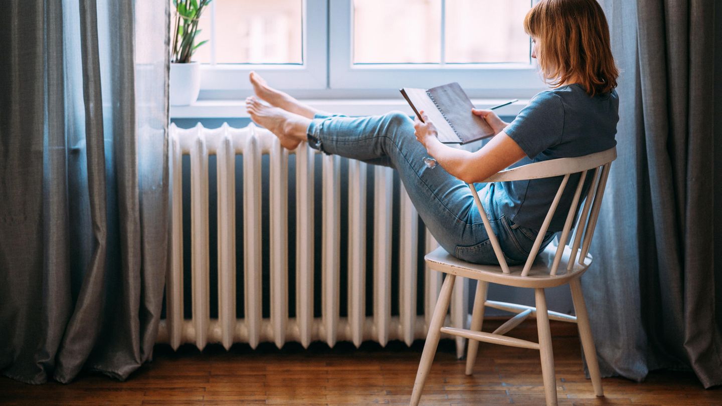Eine junge Frau mit roten Haaren sitzt am Fenster und schreibt in ein Buch