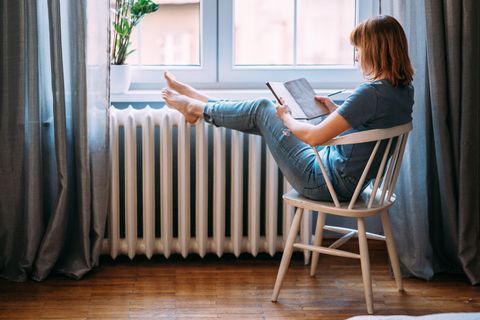 Eine junge Frau mit roten Haaren sitzt am Fenster und schreibt in ein Buch