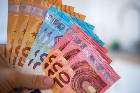 Die linke Hand einer Frau hält aufgefächert 10-, 20- und 50-Euro-Scheine