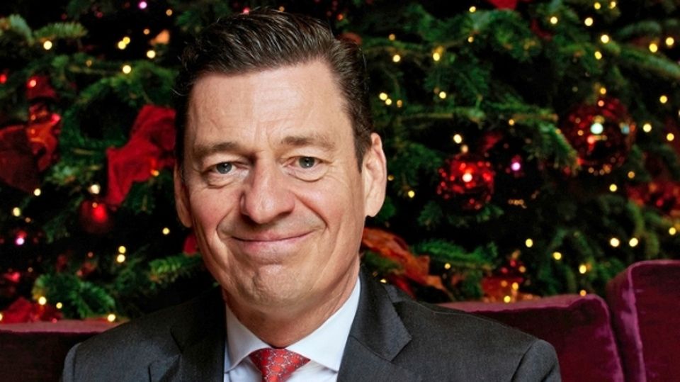 Hoteldirektor Ingo C. Peters sitzt vor einem Weihnachtbaum und lächelt