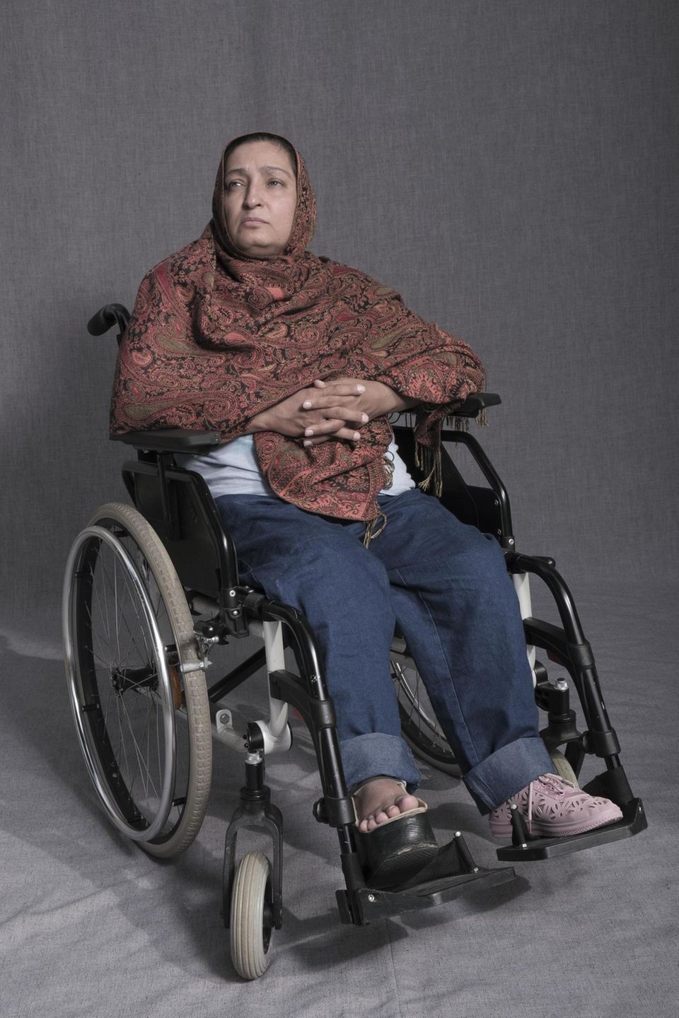 Maliha Jami in ihrem Rollstuhl, die Hände auf dem Bauch gefaltet