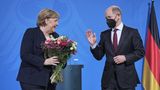 Merkel hält Blumen in den Händen - Scholz hebt die Hand zum Dank
