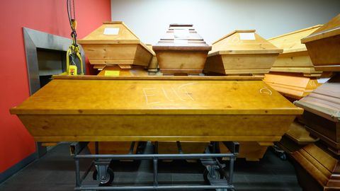 Helle Holzsärge stehen mit Kreide beschriftet in einem Krematorium