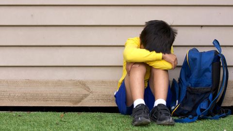 Ein von Mobbing betroffenes Kind sitzt an einer Hauswand