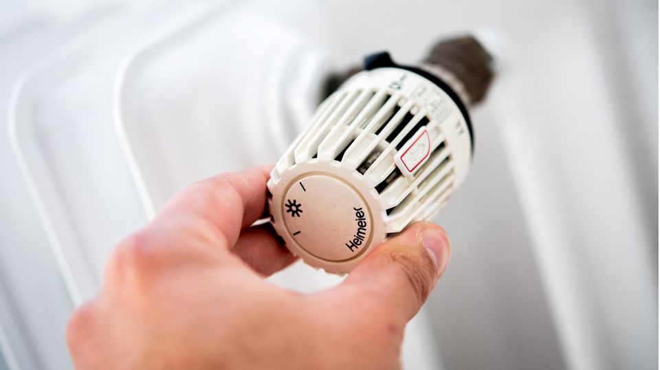 Eine Hand dreht an dem Thermostat einer Heizung