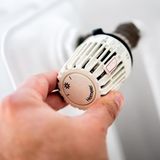 Eine Hand dreht an dem Thermostat einer Heizung