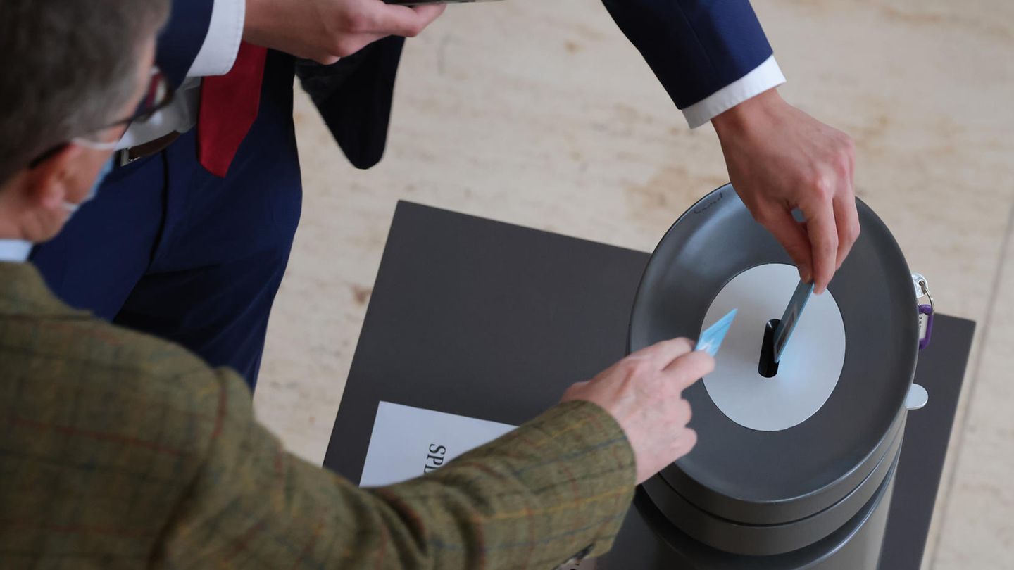 Zwei Männer in Anzügen werfen ihre Abstimmungskarten in eine Wahlurne im Bundestag