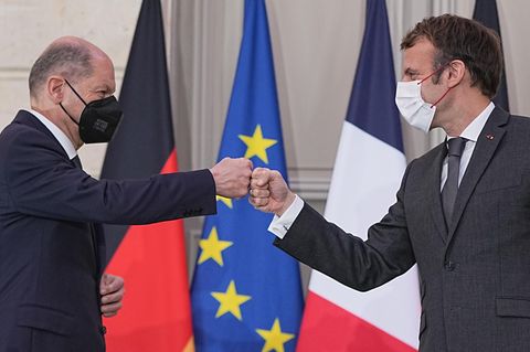Zwei weiße Männer in Anzügen und mit FFP2-Masken begrüßen sich Faust an Faust