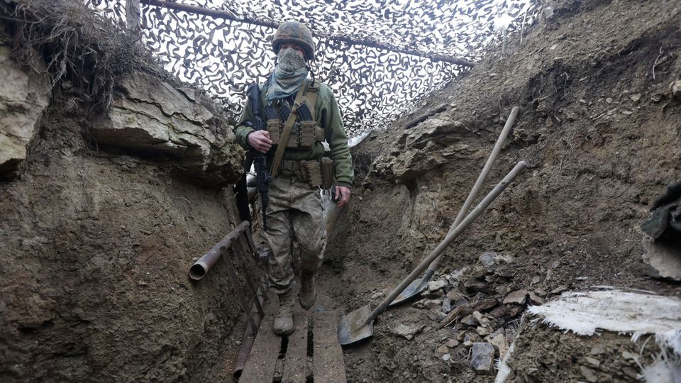 Ukrainischer Soldat in einem mit Tarnnetz überspannten Schützengraben