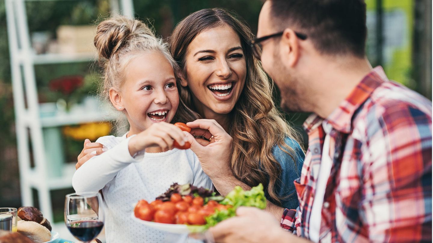 Eine Frau, ein Mädchen und ein Mann lachen gemeinsam. In ihrer Mitte ein Teller voll Gemüse.