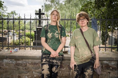 Zwei Frauen stehen in Schlamm verdreckter Kleidung an eine Mauer gelehnt