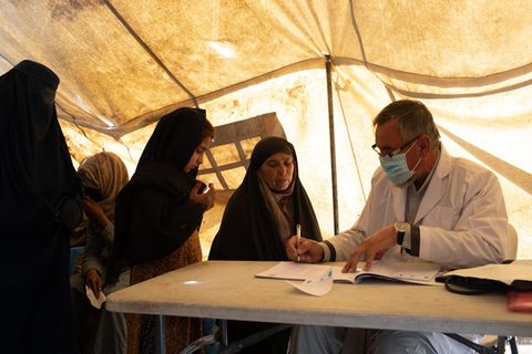 Ein Mann in weißem Kittel sitzt mit mehreren Frauen an einem Tisch