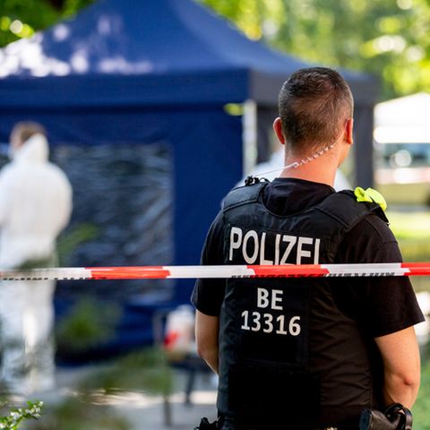 Ein Polizeibeamter und Mitarbeiter der Spurensicherung, im Hintergrund ein blaues Zelt