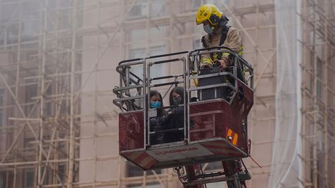Mit einem Rettungskorb an einer Feuerwehrleiter bringt ein Feuerwehrmann in Uniform zwei Frauen in Sicherheit