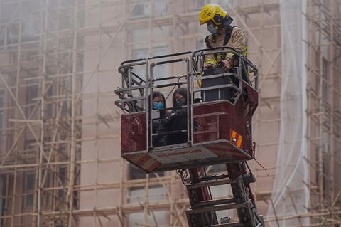 Mit einem Rettungskorb an einer Feuerwehrleiter bringt ein Feuerwehrmann in Uniform zwei Frauen in Sicherheit