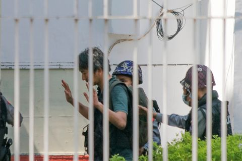 Mann wird von Polizeibeamten hinter Gitterzaun abgeführt