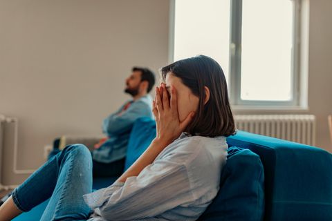 Frau und Mann sitzen voneinander abgewendet auf dem Sofa. Frau hält sich die Hände vor das Gesicht