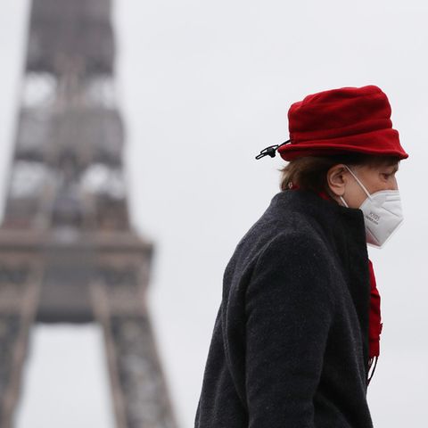 Eine Frau mit rotem Hut läuft am Eiffelturm in Paris vorbei