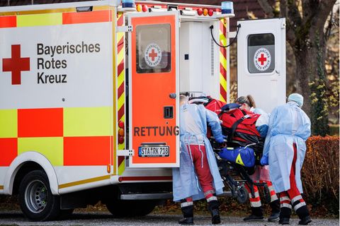 Drei Menschen in Schutzkleidung laden einen Corona-Intensivpatienten in das Heck eines Rettungswagens des Bayrischen Roten Kreuz