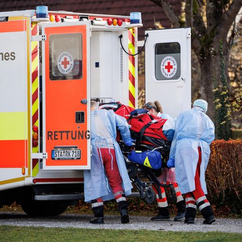 Drei Menschen in Schutzkleidung laden einen Corona-Intensivpatienten in das Heck eines Rettungswagens des Bayrischen Roten Kreuz