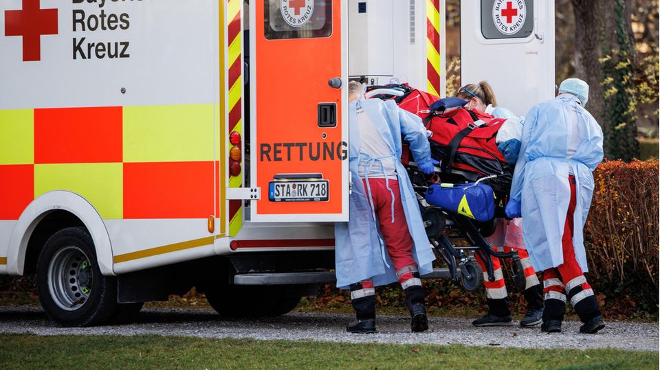 Drei Menschen in Schutzkleidung laden einen Corona-Intensivpatienten in das Heck eines Rettungswagens des Bayrischen Roten Kreuz