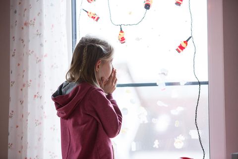 Ein kleines Mädchen steht vor einem Fenster und schaut hinaus