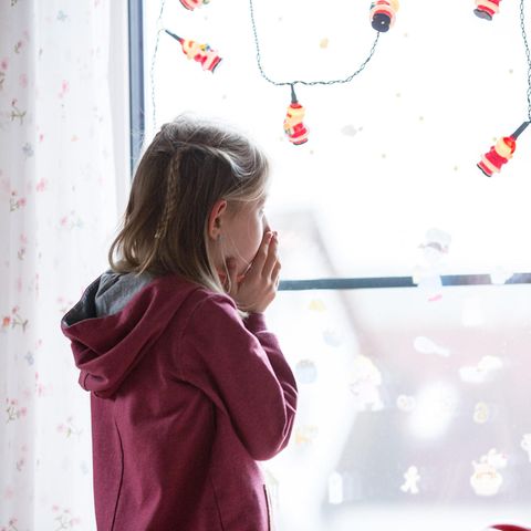 Ein kleines Mädchen steht vor einem Fenster und schaut hinaus