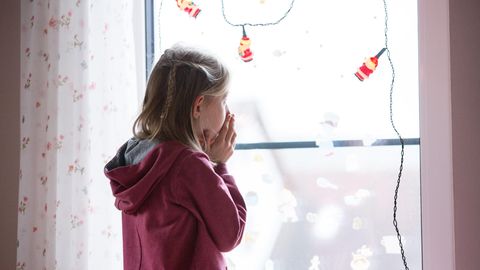 Ein kleines Mädchen steht vor einem Fenster und schaut hinaus