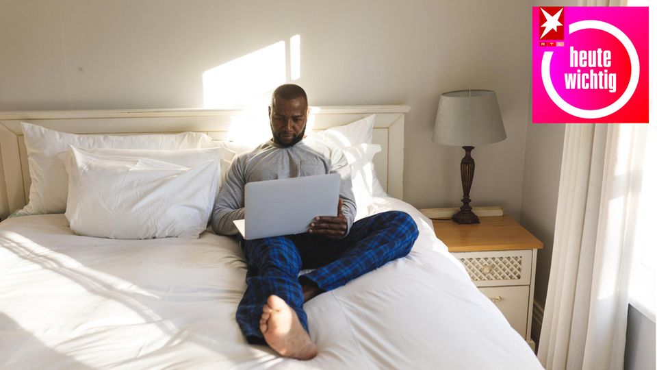 Ein Mann sitzt mit Laptop auf einem Bett