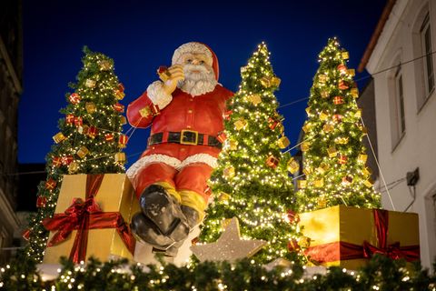 Ein Weihnachtsmann, Geschenke und kleine Weihnachtsbäume schmücken einen Stand auf einem Weihnachtsmarkt