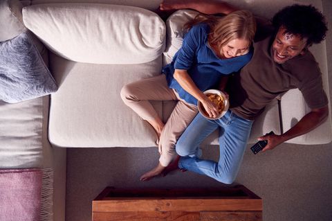 Ein Paar sitzt auf dem Sofa, eine Schüssel mit Chips vor sich