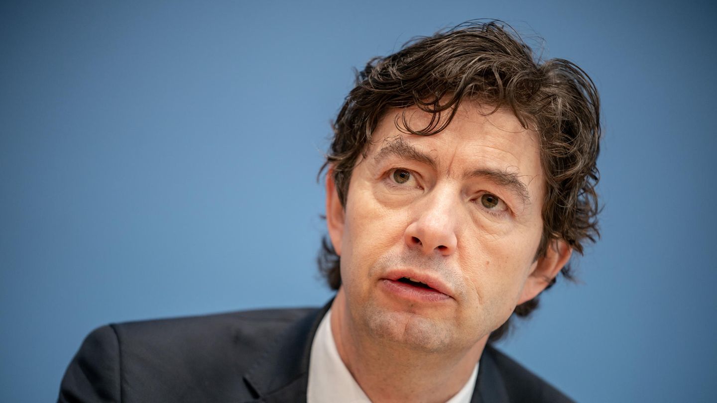 Christian Drosten sitzt im Anzug vor einer blauen Wand