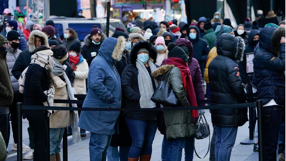 In Winterkleidung und mit OP-Masken stehen Menschen in New York in einer mit Abesperrbändern geordneten Warteschlange