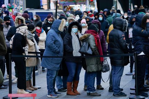 In Winterkleidung und mit OP-Masken stehen Menschen in New York in einer mit Abesperrbändern geordneten Warteschlange