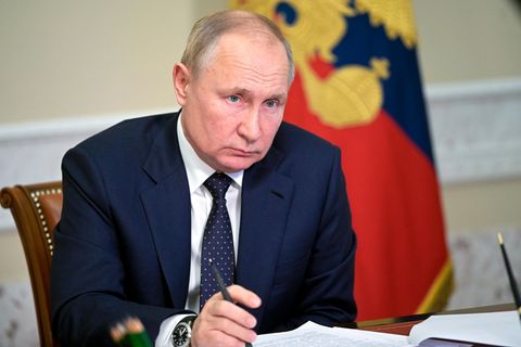 Ein älterer weißer Mann im Anzug sitzt an einem Schreibtisch, hinter dem eine russische Flagge hängt