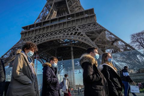 Menschen mit Masken laufen in Paris am Eiffelturm vorbei